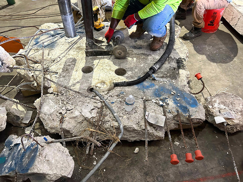 Workers drilling into a piece of concrete with rebar sticking out during a safety investigation