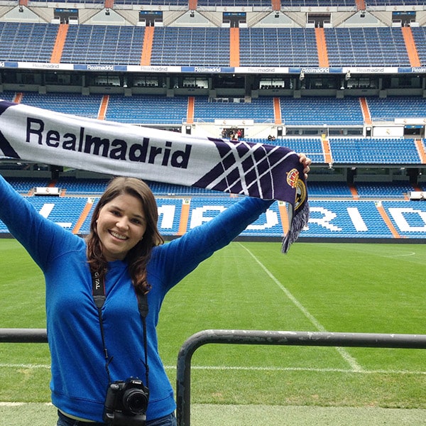 A student holds a scarf with RealMadrid above her head in the Santiago Bernabeu Stadium with the field in the background