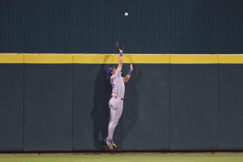 Hayden Yost in a Gator baseball uniform jumps to catch a ball at the outfield wall during a game.