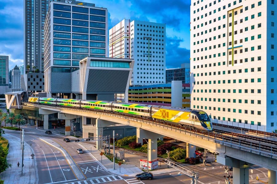 A passenger train departs MiamiCentral on an elevated track with tall buildings all around