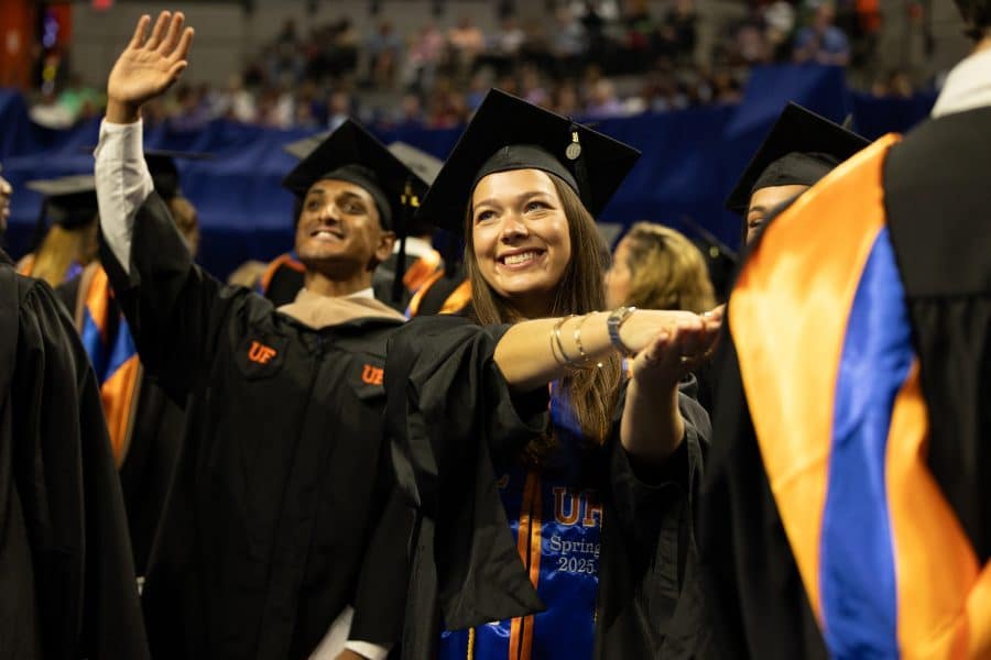Students in graduation regalia celebrate their commencement in the Stephen O'Connell Center. One student performs the Gator chomp while another waves in the background surrounded by their peers.