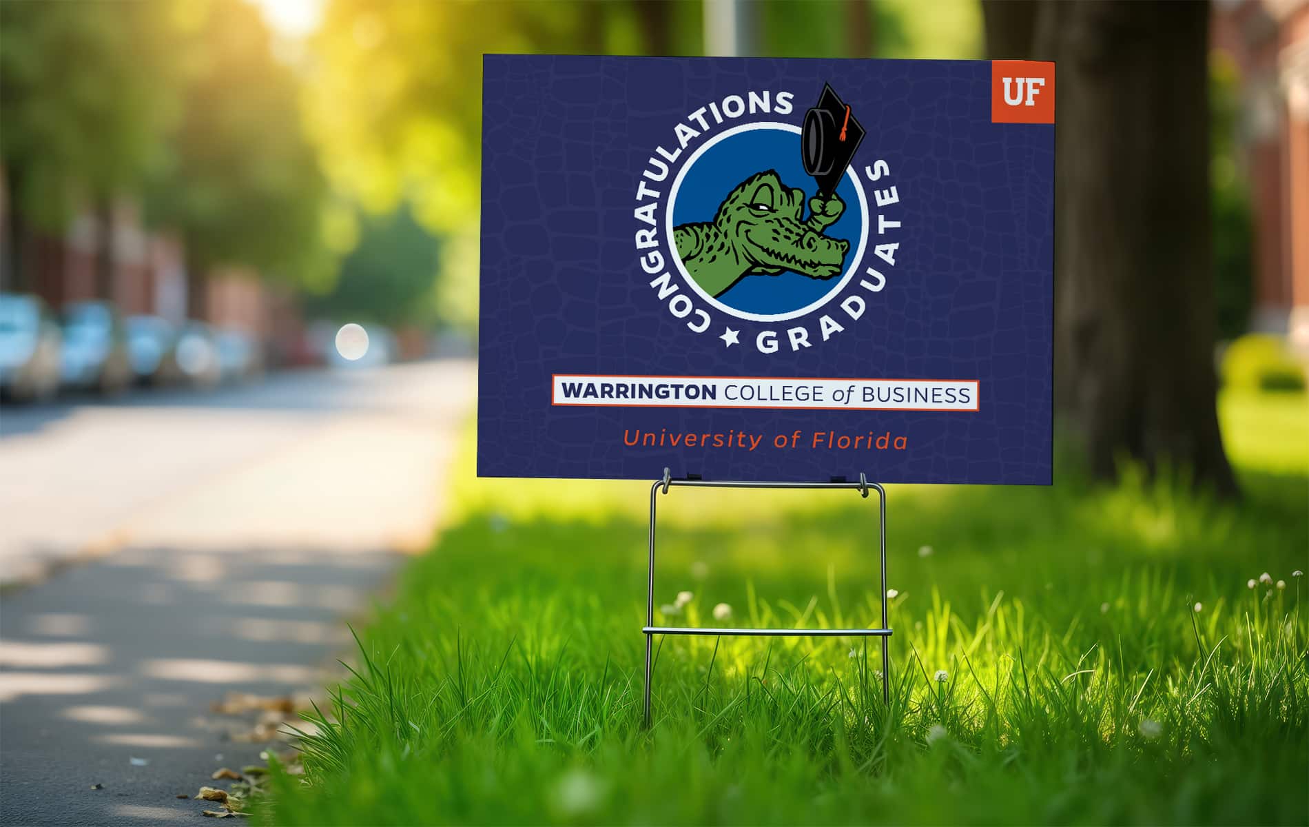 A lawn sign staked in grass featuring the UF alligator wearing a graduation cap and the text “Congratulations Graduates” above “Warrington College of Business – University of Florida.”