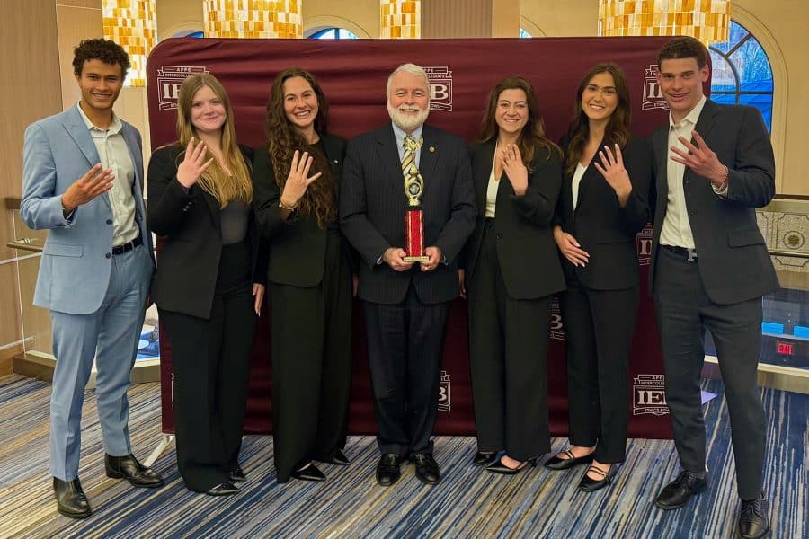 Ethics competition team holding up the number four with their fingers with brian ray holding a trophy