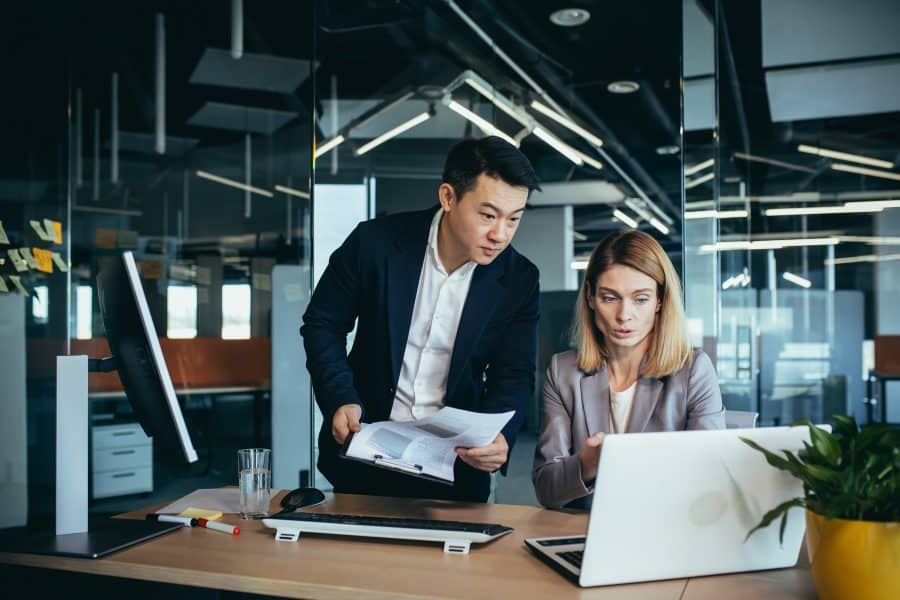 Two employees in a modern office, an Asian man and a woman working at a table, colleagues discussing and consulting, thinking about a joint project