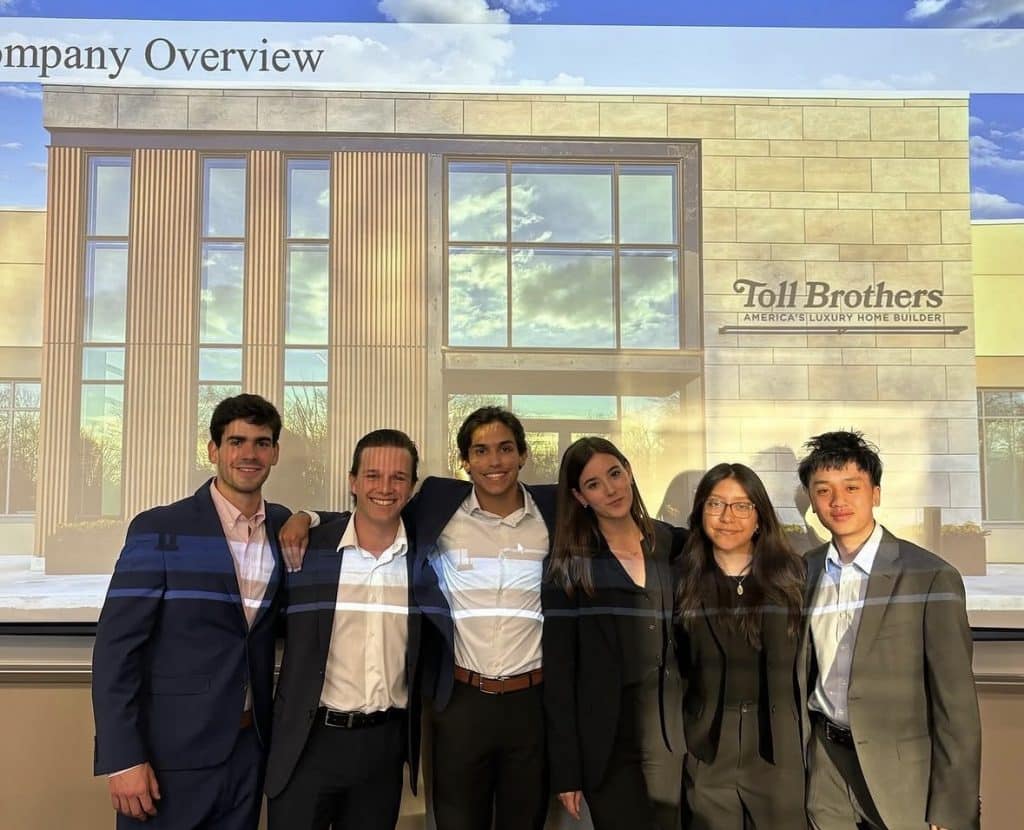 Alejandra poses with peers in front of a presentation on Toll Brothers.