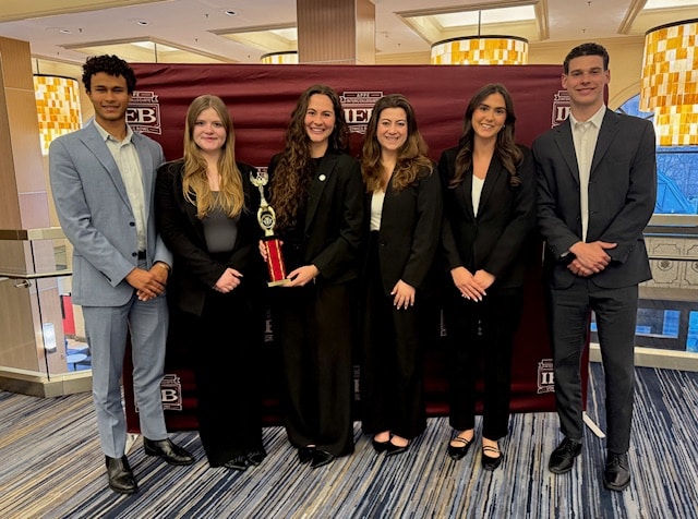 uf business ethics case competition team standing in front of a backdrop with their hands folded, smiling and holding a trophy