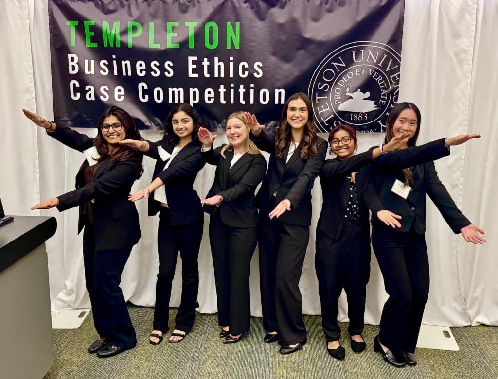 uf ethics case competition team smiling and doing the gator chomp in front of business ethics case competition sign