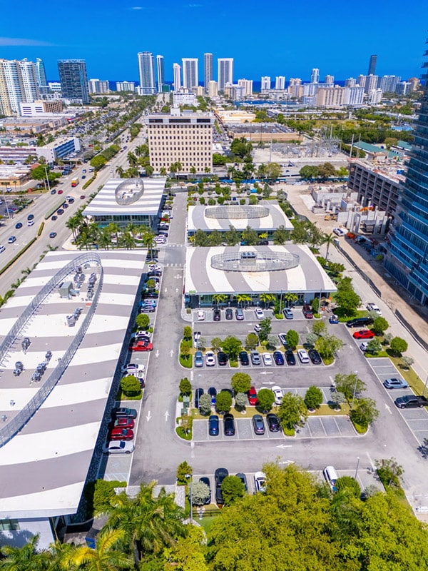 A high vantage point of a coastal city with buildings, palm trees and tall resorts with an ocean in the distance.