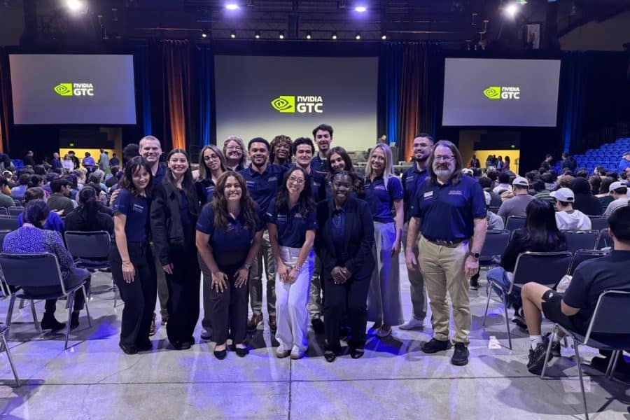 A group of about 20 students stand in front of a presentation screen for NVIDIA.