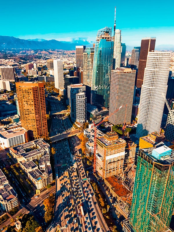 High vantage point view of Los Angeles tall buildings and traffic below with mountains in the background.