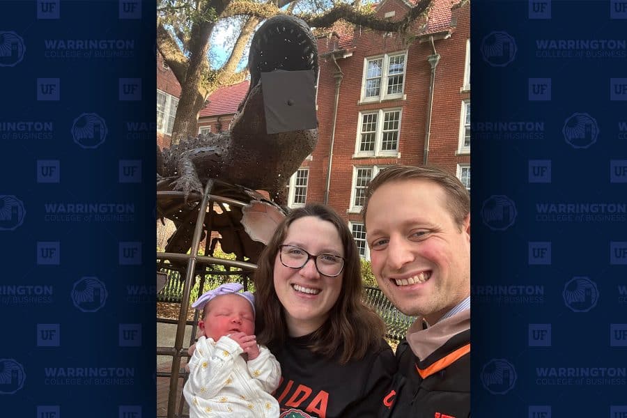 matthew brown and katie mazzola holding baby florence and smiling in a selfie in front of the heavener gator globe statue