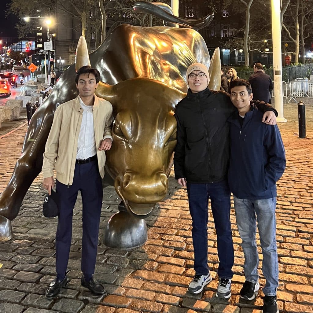 Amay Mehta, Kaushal Naidu, and Nguyen Khang Do standing in front of a golden bull statue smiling
