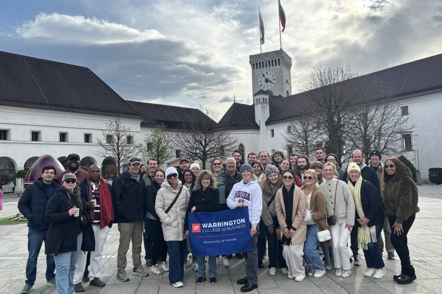 MBA students pose for a group photo in front of a building on the Croatia Global Immersion Experience. One student holds a banner that says "Warrington College of Business, University of Florida."