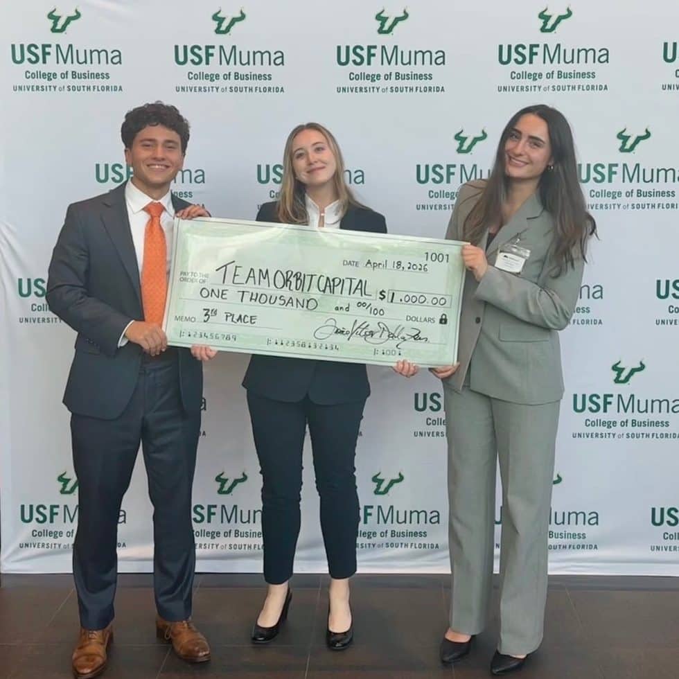 Sophia Miele, Catheirne McGarry and Daneil Khani holding up a one thousand dollar check smiling in front of a USF Muma sign