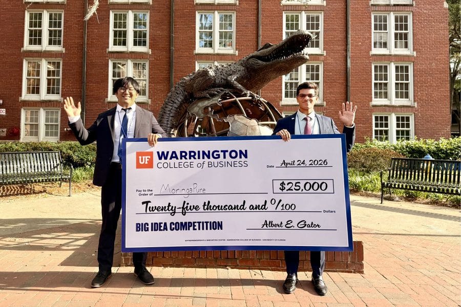 Abhith Kasala and Kallum Wang holding up a check for $25,000 and waving in front of the Hevener Gator Globe statue