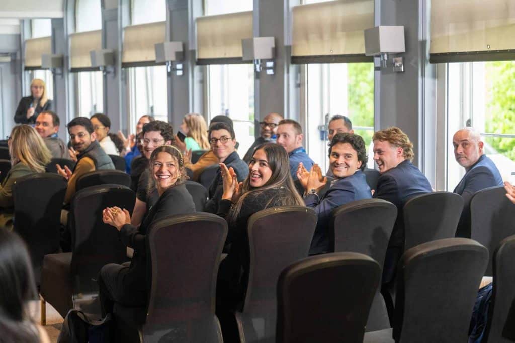 university of glasgow mib team sitting in a row of chairs with their heads turn, smiling and clapping