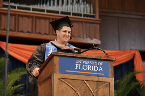 MBA alumni Joseph Arrunategui in a cap and gown speaking on a University of Florida podium