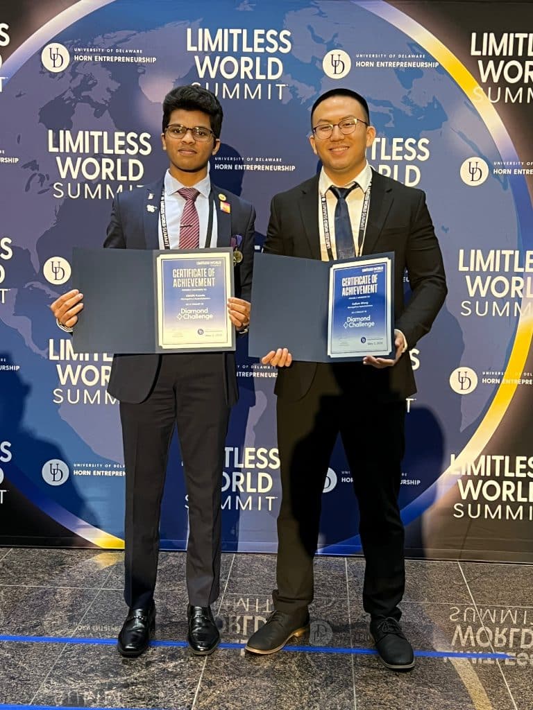 Abhith Kasala and Kallum Wang standing and holding certificate of achievement in front of a limitless world summit sign