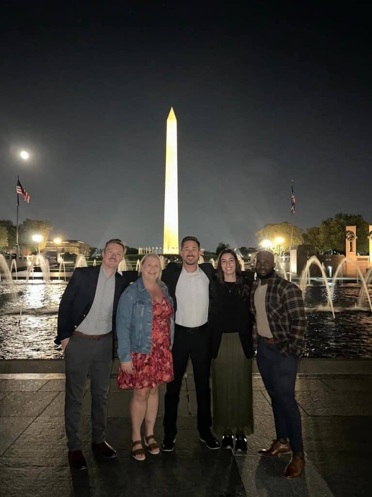 Taylor smith and team standing in smiling at night in front of the Washington monument