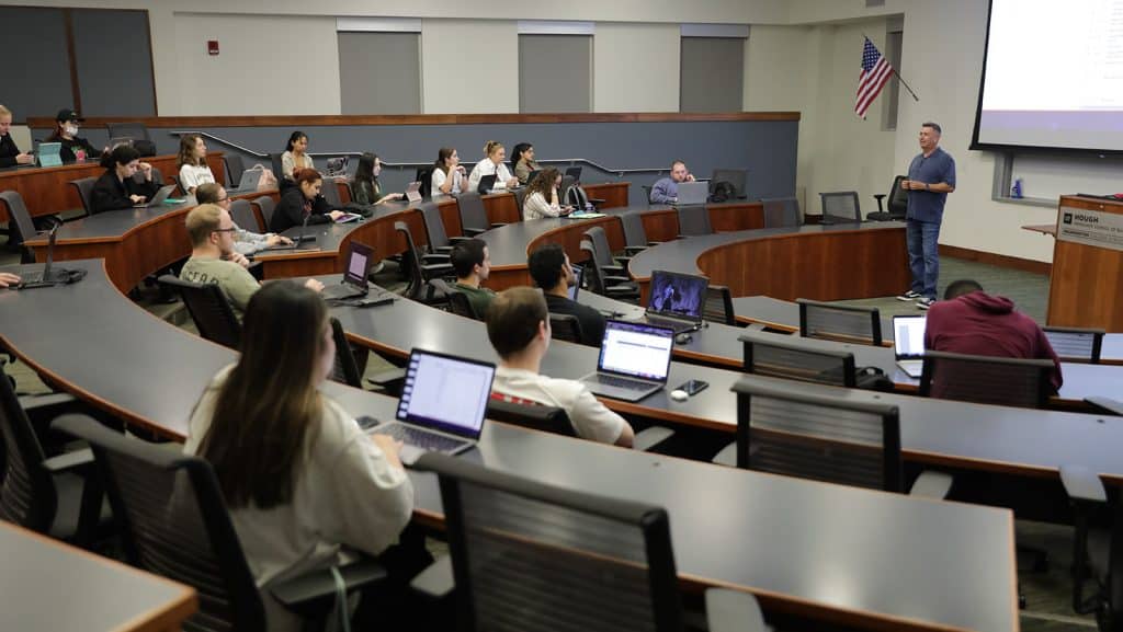 Students seated in a Hough Hall classroom listen to Mike Carrillo as he stands at the front of the room.