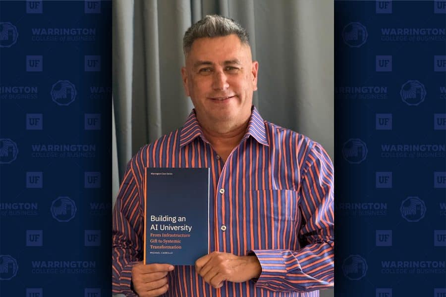 Michael Carrillo stands holding a copy of the first Warrington Case Series case, Building an AI University: From Infrastructure Gift to Systemic Transformation.