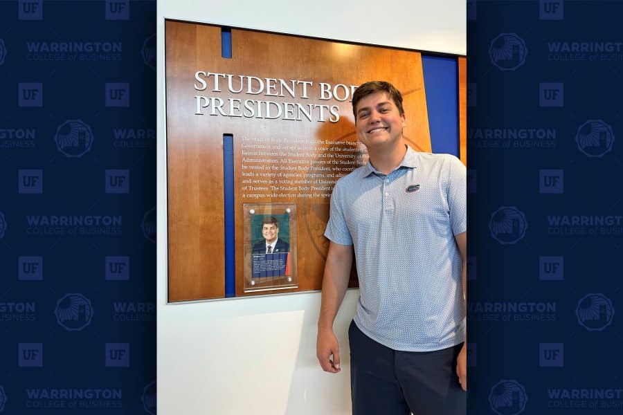 Blake Cox poses in front of a sign that says "Student Body President." The sign has a placard with his name, photo, the year 2025-2026, and information about him.