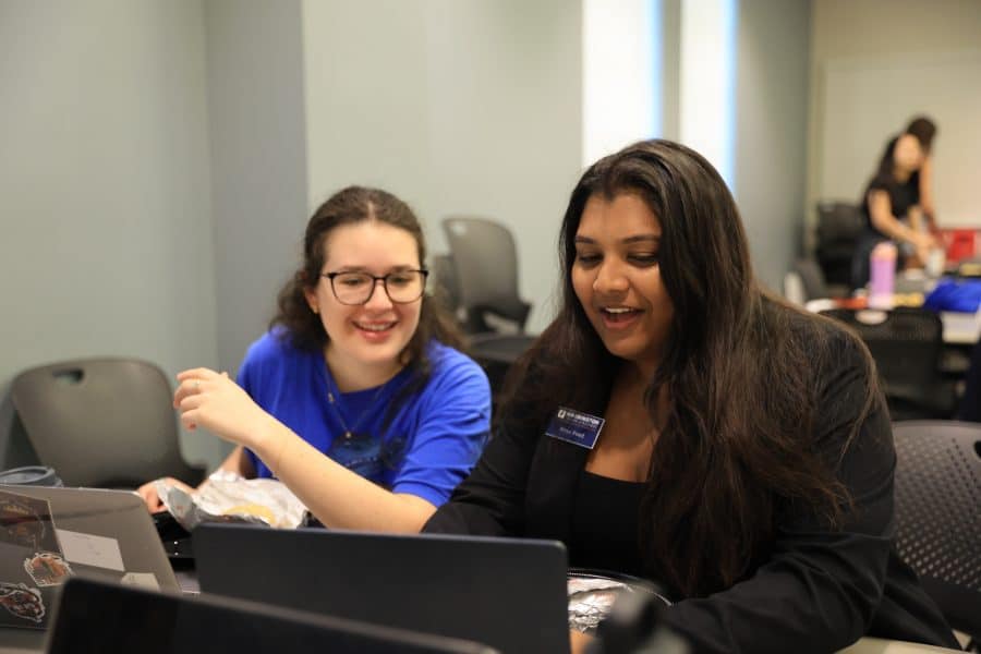 First-Gen Fellowship program facilitator Priya Patel shows a fellow something on her computer in a classroom.