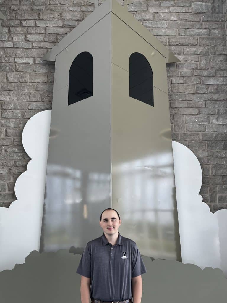 Bryce Gillingham stands in front of a large gray tower, the logo of Tower Hill Insurance.
