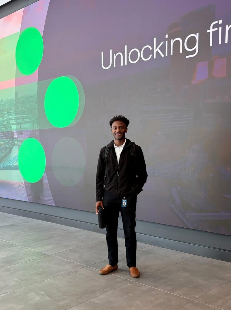 Kelly Kemari stands in front of a wall that reads "Unlocking finance" with the letters "a,n,c,e" out of frame.