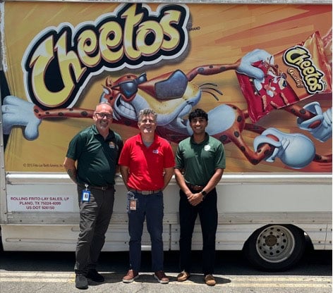 Jeremy Thomas stands with two other men in front of a Cheetos delivery truck.