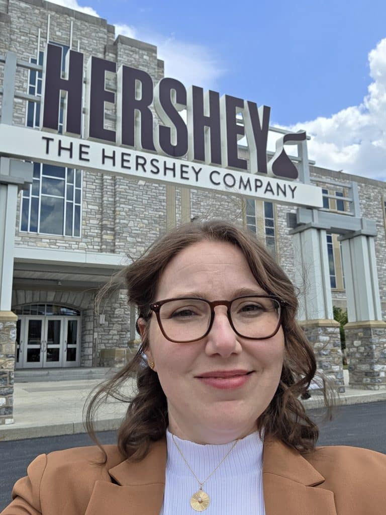 Kate Bennett takes a selfie in front of the Hershey Chocolate Company building on a sunny day. 