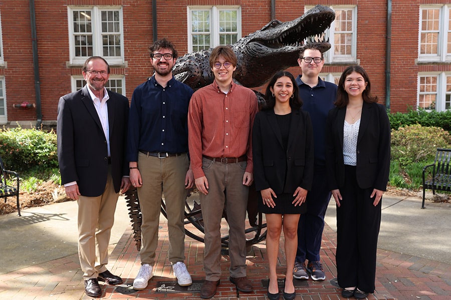 The Director of the Public Utility Research Center, Dr. Mark Jamison, and students doing research for the center stand in front of the Gator Ubiquity Statue.