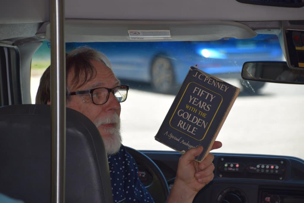 A man holds a up a copy of JC Penney's book Fifty Years within the Golden Rule: A Spiritual Awakening.