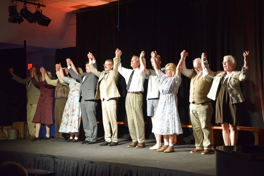 A cast of about 10 actors stands on stage while holding hands before taking a bow.
