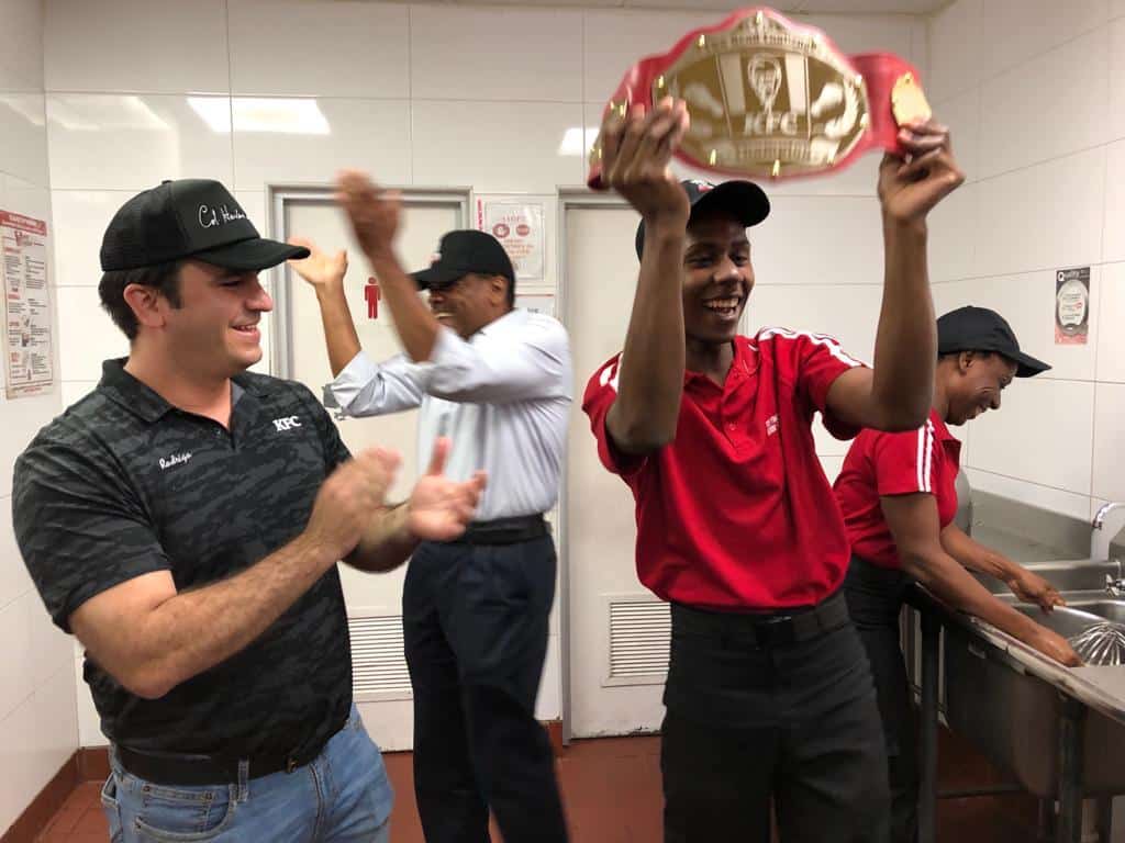 Four men cheer while one holds up a championship boxing belt.